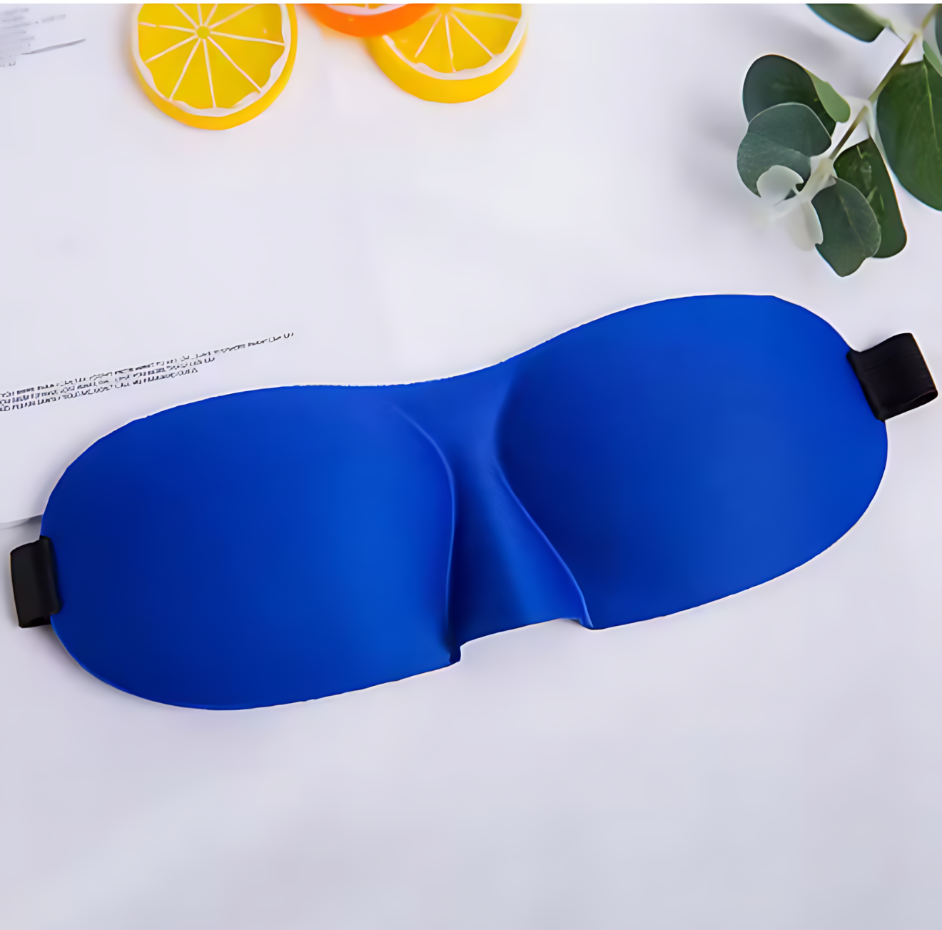 Blue sleep mask on a white surface with orange slices and green leaves.